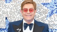 Image of Elton John standing and smiling with sunglasses on