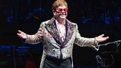 Elton John standing onstage with his arms open
